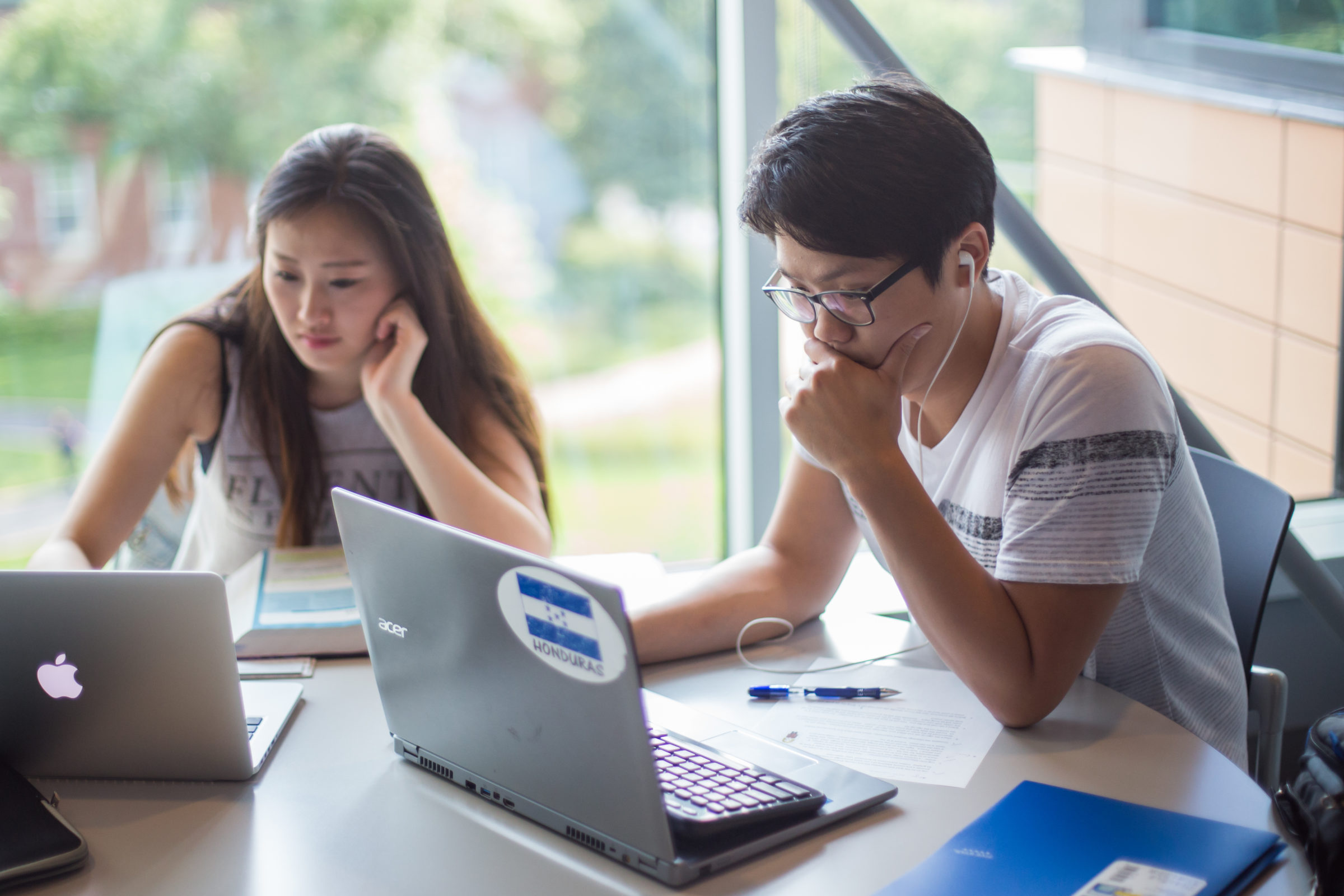 Two students study together at a table with their silver laptops.