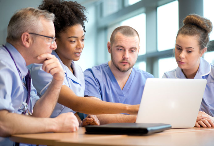 Nursing students crowd around a laptop.