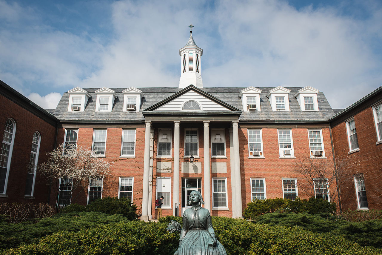 External view of Nyvall Hall Seminary building. Statue of Swedish woman and green bushes cover the ground in front of Red brick building with white steeple.