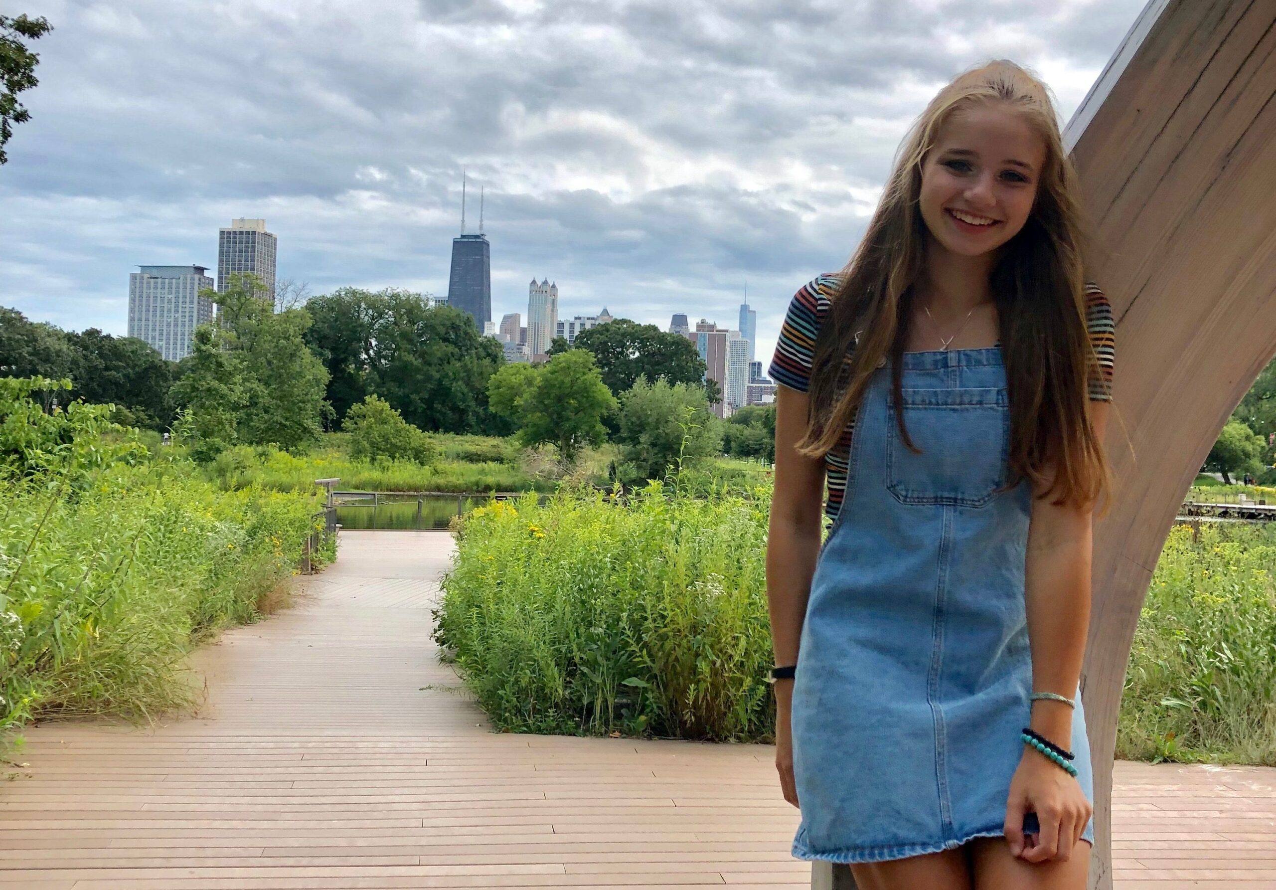 A young woman standing on a park pathway with the Chicago skyline behind her.