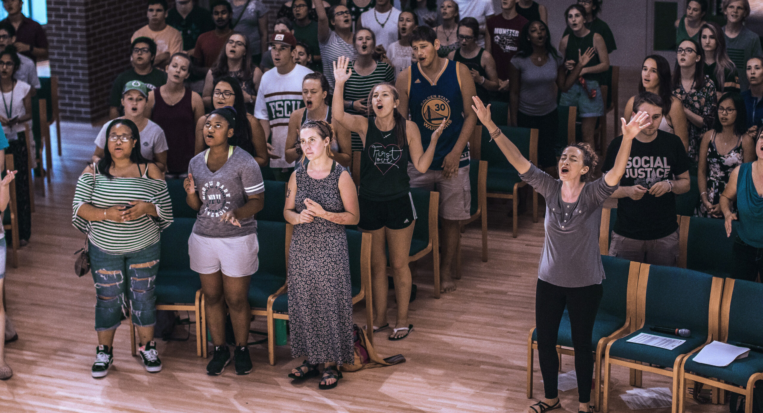 Students gathered in chapel sing and raise hands in worship.