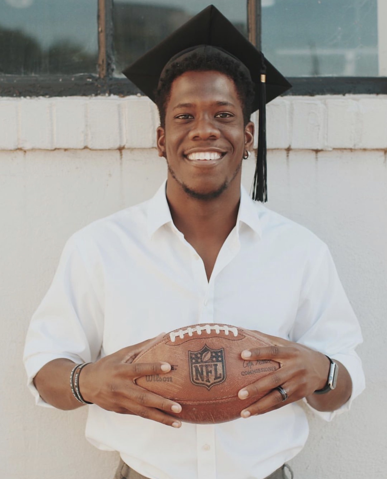 Male student in graduation cap holds football.