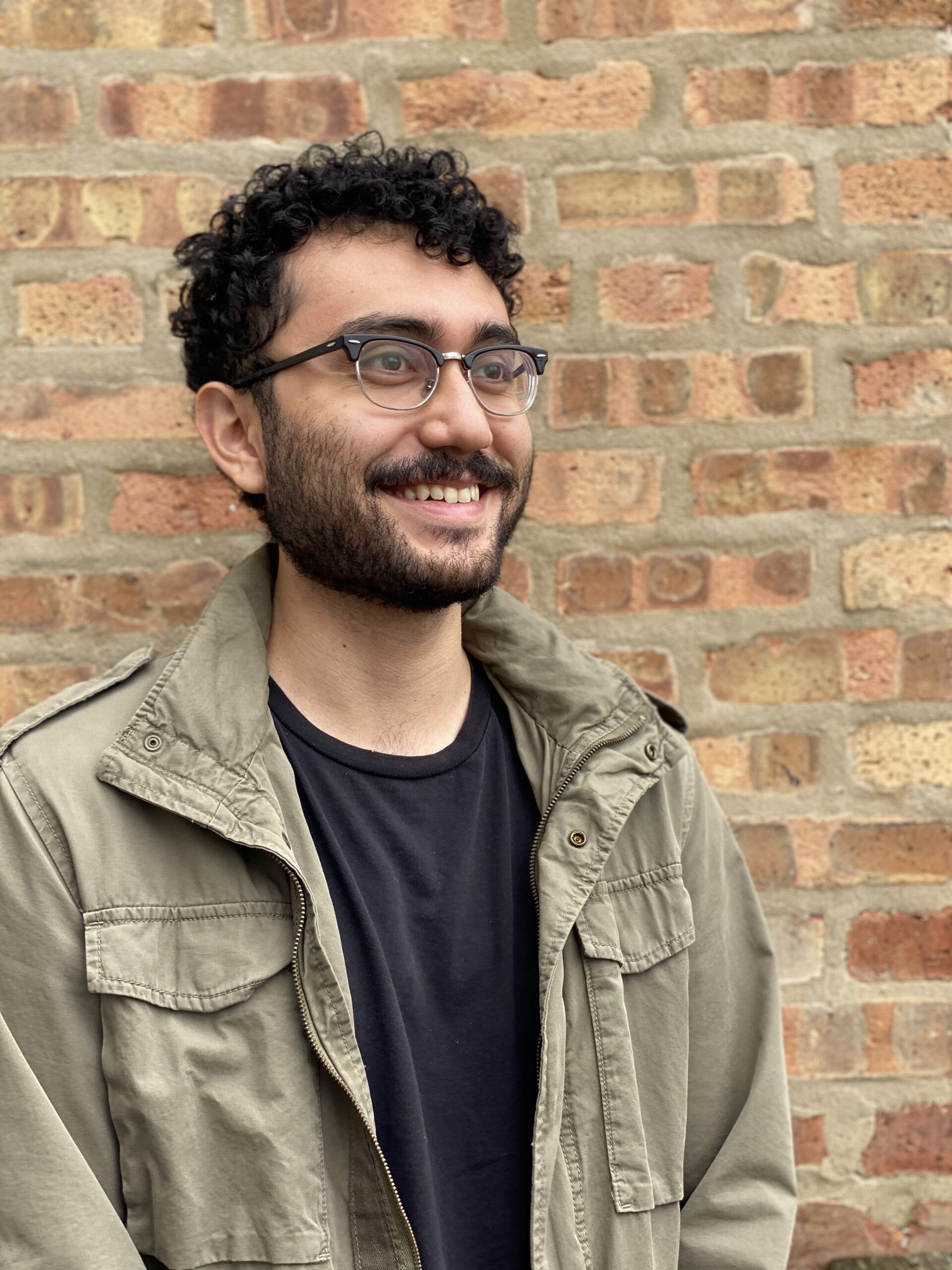 Student in green cargo jacket stands in front of brick wall.