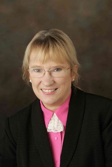 Smiling woman in black suit, pink collar, and glasses