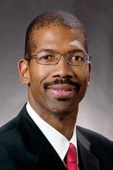 Smiling man in black suit, red tie, and glasses