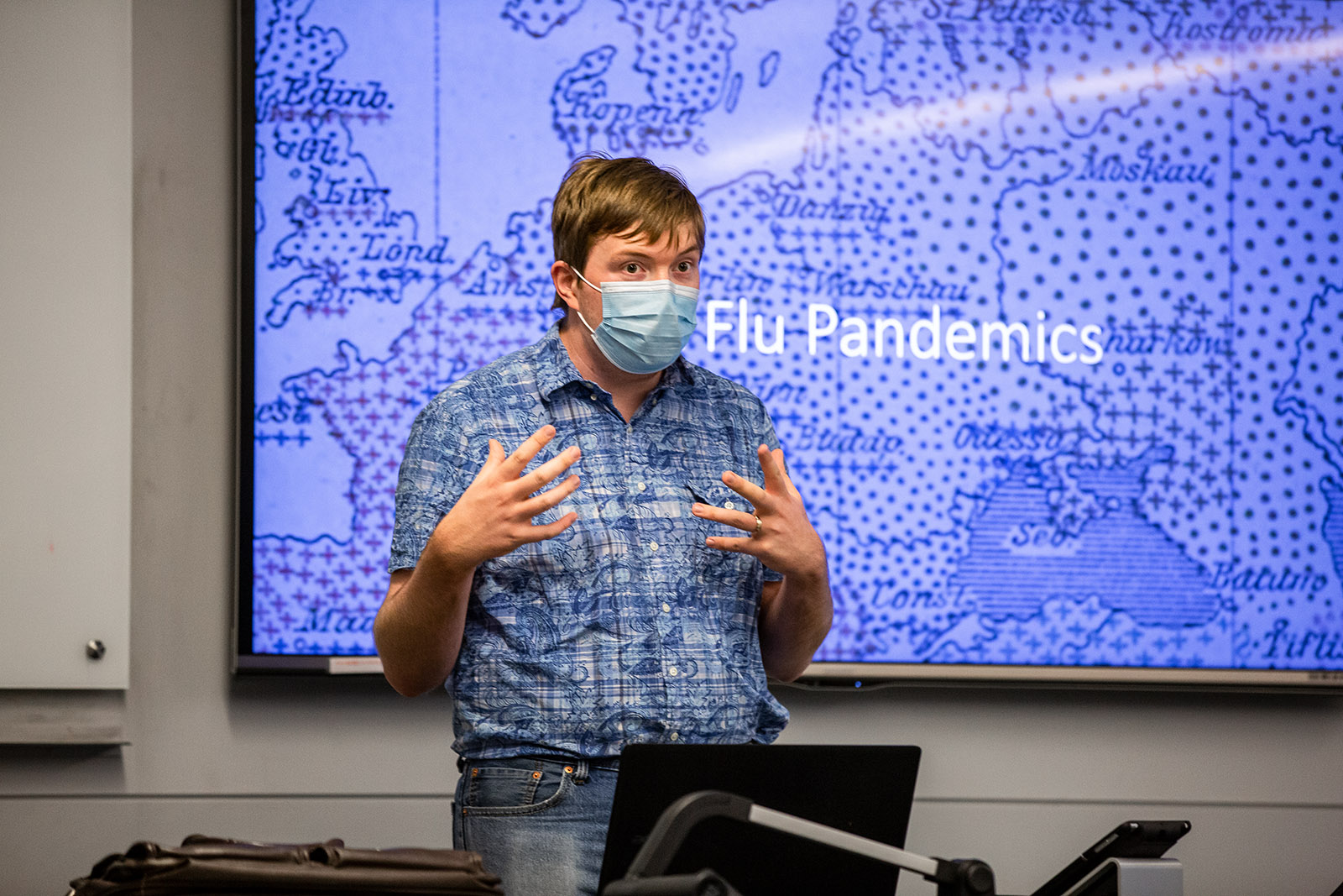 Professor wearing cloth face mask lectures with powerpoint slide showing map of "Flu Pandemics"