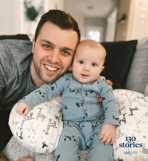 man and baby smile while sitting on living room sofa.