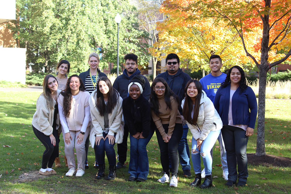 group of students and professor stand under autumn trees