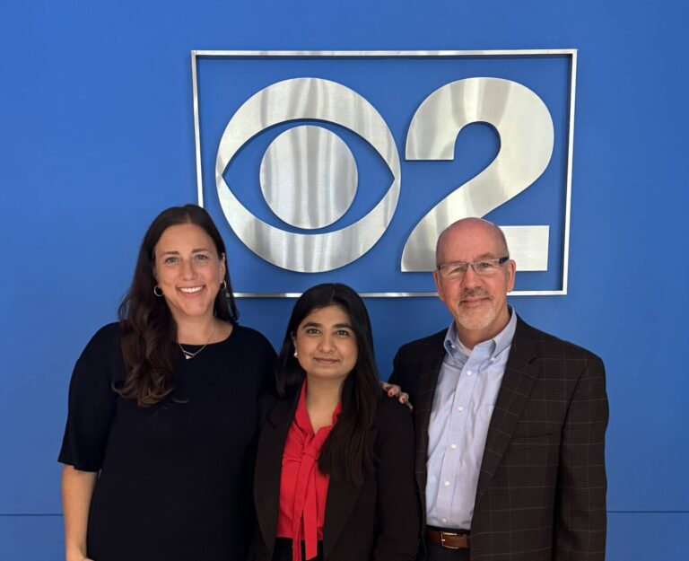 Three individuals posing in front of the CBS Chicago logo.