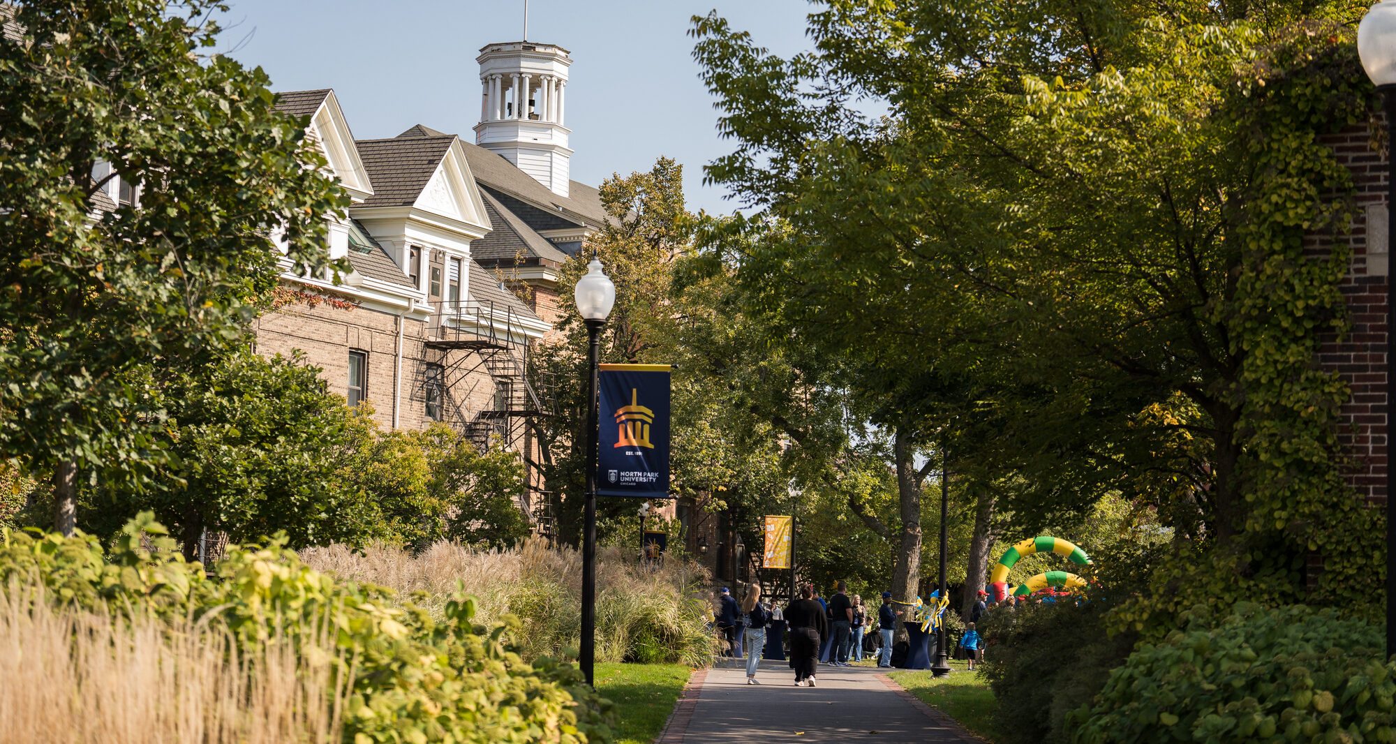 Campus greenery with the Old Main building and homecoming celebration off in the distance